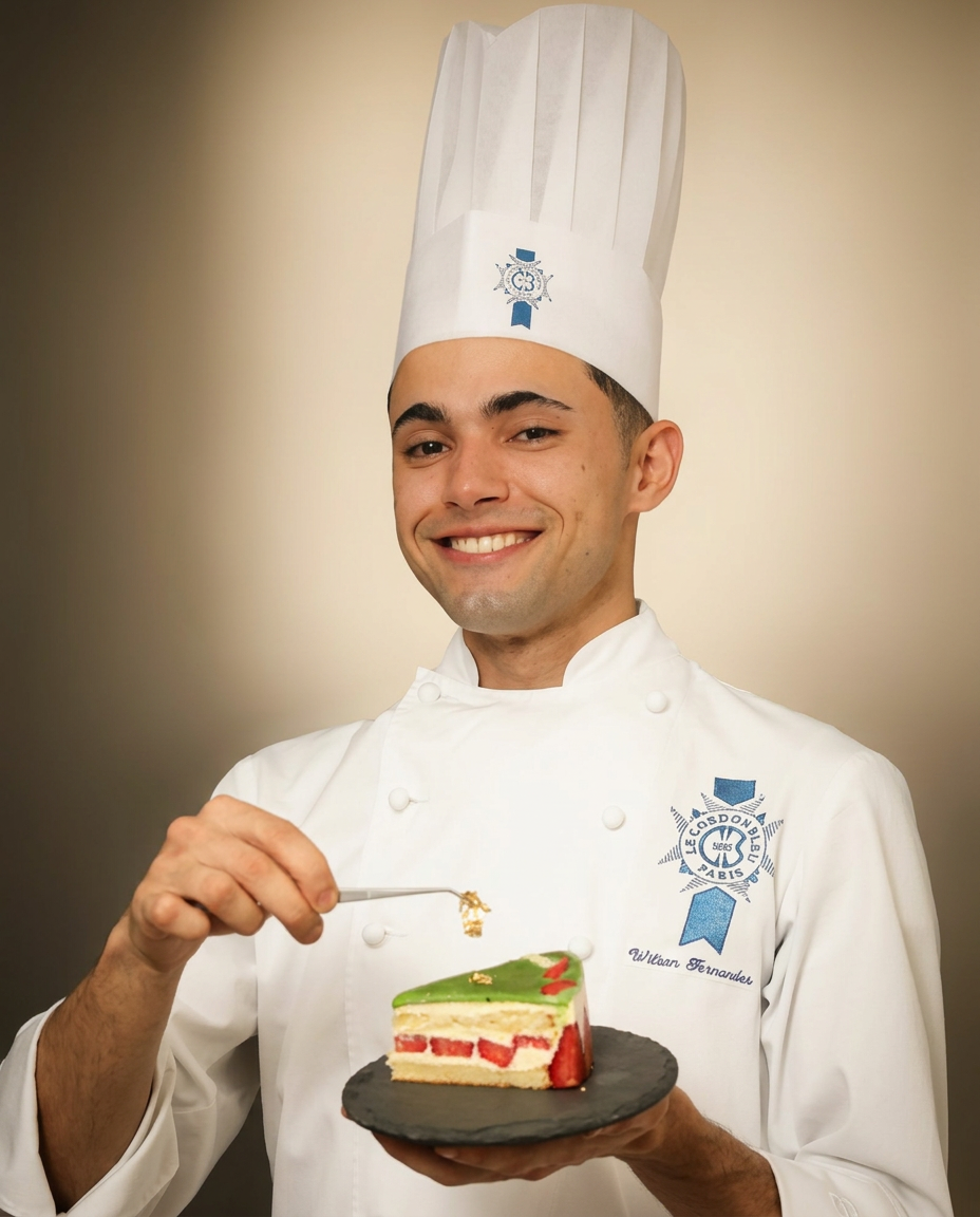 Chef Wilson Fernandes em uniforme do Le Cordon Bleu segurando uma fatia de bolo decorada